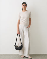 Person standing with handbag wearing short-sleeve shirt and wide-leg pants.