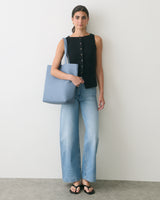 Person standing with tote bag, wearing sleeveless top and jeans.