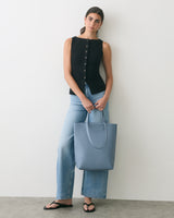 Person standing with a handbag, wearing a sleeveless top, jeans, and sandals.