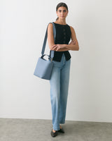 Person standing with a handbag, wearing jeans and a sleeveless top.