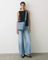 Person wearing a sleeveless top and wide-leg jeans, holding a shoulder bag.