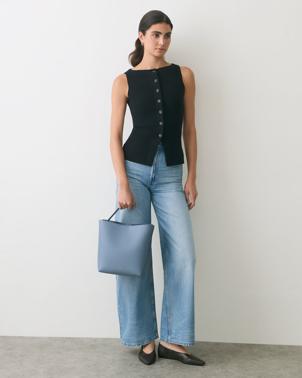 Person wearing a sleeveless top and wide-leg jeans holding a bag.