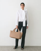 Person in white shirt and dark pants holding a handbag, standing against a plain background.