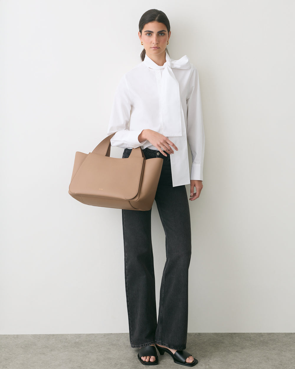 Person standing with a handbag, wearing a blouse and pants.