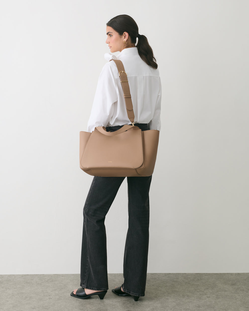 Person standing sideways holding a travel bag over shoulder.
