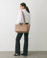 Person standing sideways holding a travel bag over shoulder.