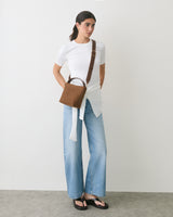 Person in jeans, shirt, and sandals with brown handbag over shoulder.