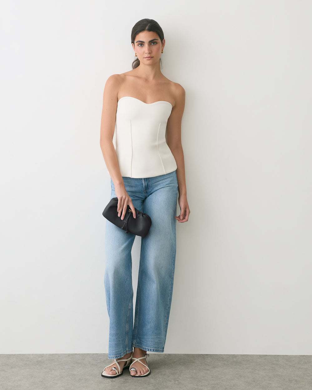 Person in a strapless top and jeans holding a clutch, wearing sandals.