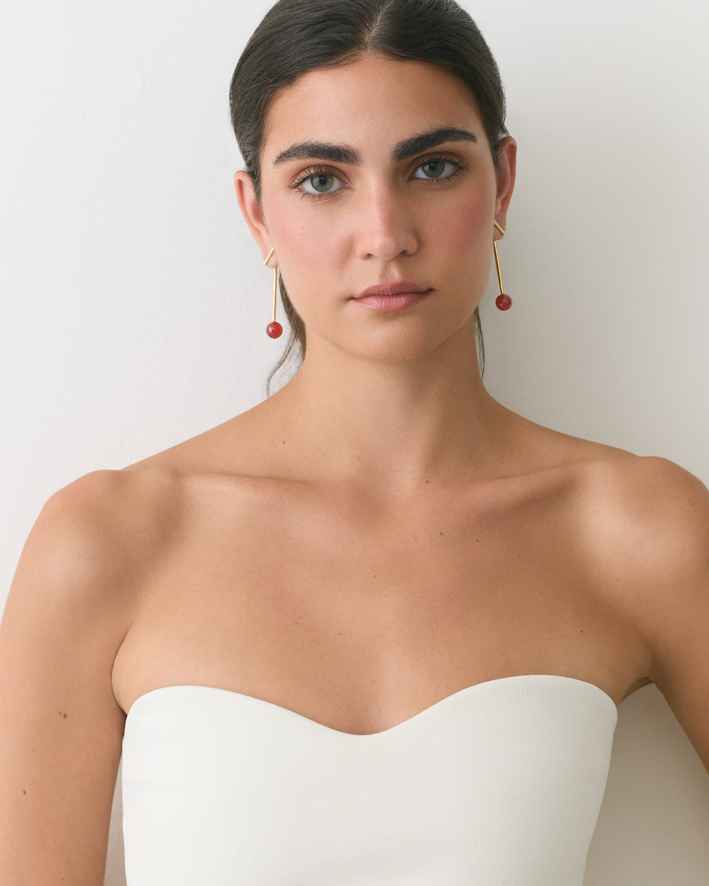 Woman wearing strapless top and dangling earrings standing against plain backdrop.