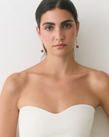 Woman wearing strapless top and dangling earrings standing against plain backdrop.
