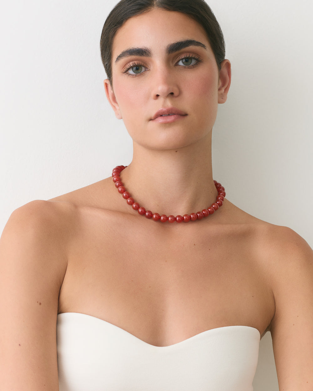 Person wearing bead necklace and strapless top with neutral expression.