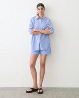 Person wearing a striped shirt and shorts, arms crossed, standing against a plain backdrop.
