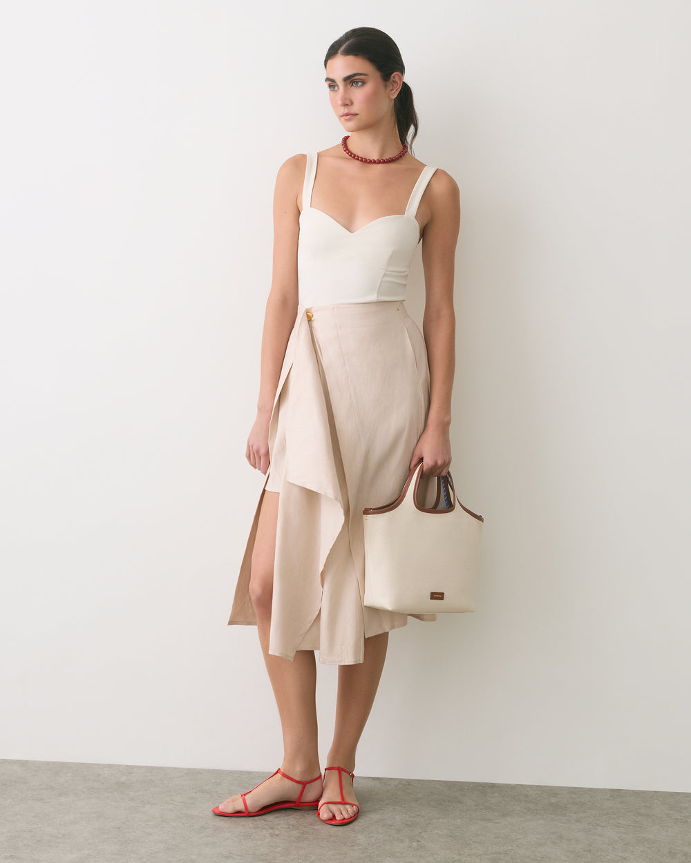 Person in a sleeveless top and layered skirt holding a handbag, wearing sandals.