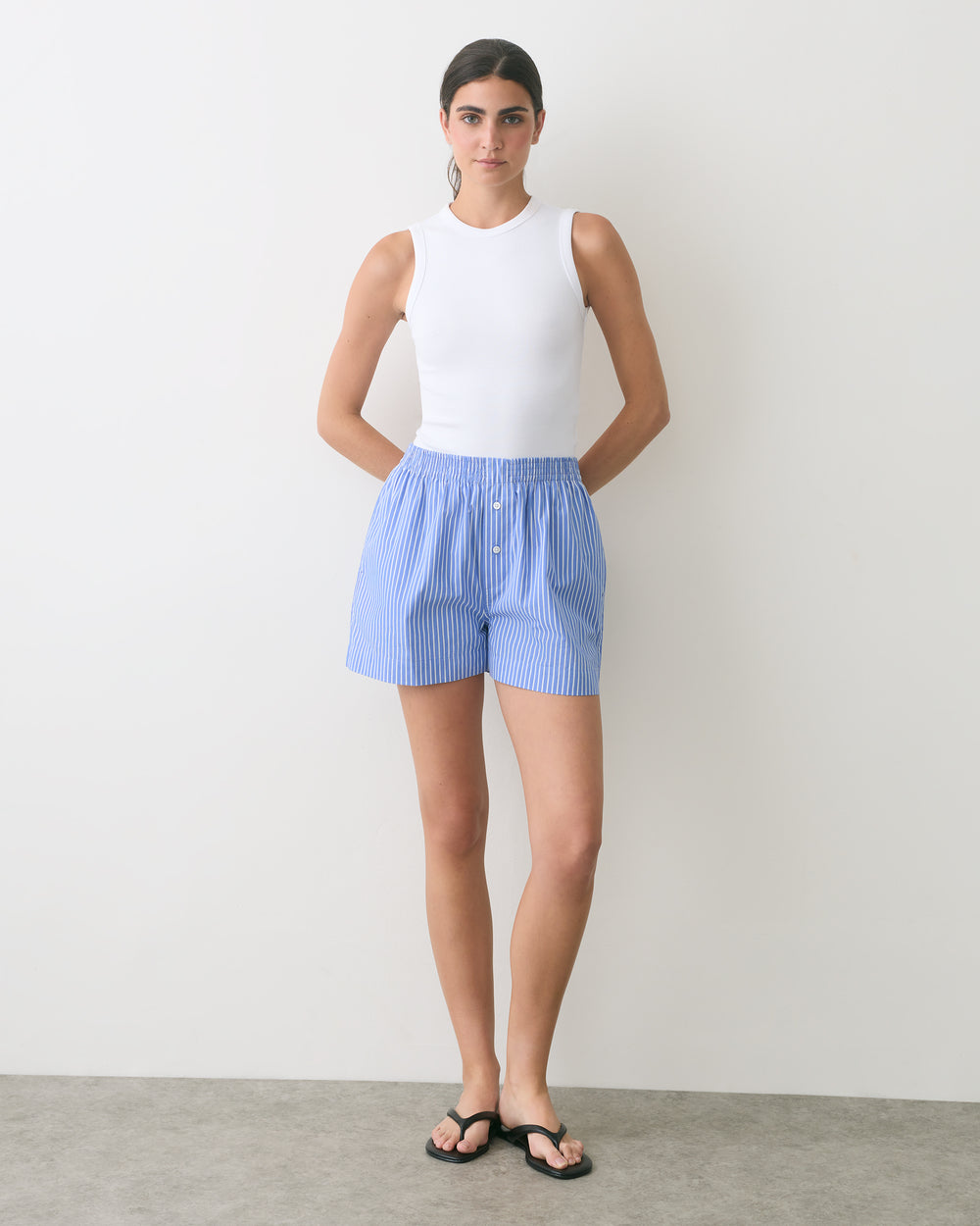 Person in sleeveless top and shorts stands with hands behind back.