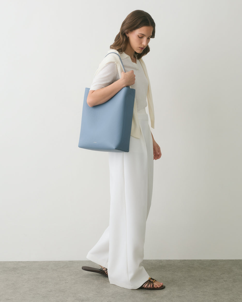 Person wearing white outfit, holding a large blue bag, standing on a gray floor.