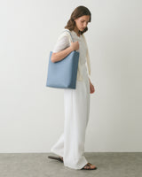 Person wearing white outfit, holding a large blue bag, standing on a gray floor.