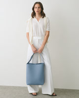 Person in white outfit holding a blue handbag in front of a plain background.