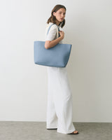 Person holding a large shoulder bag, standing sideways against a plain backdrop.