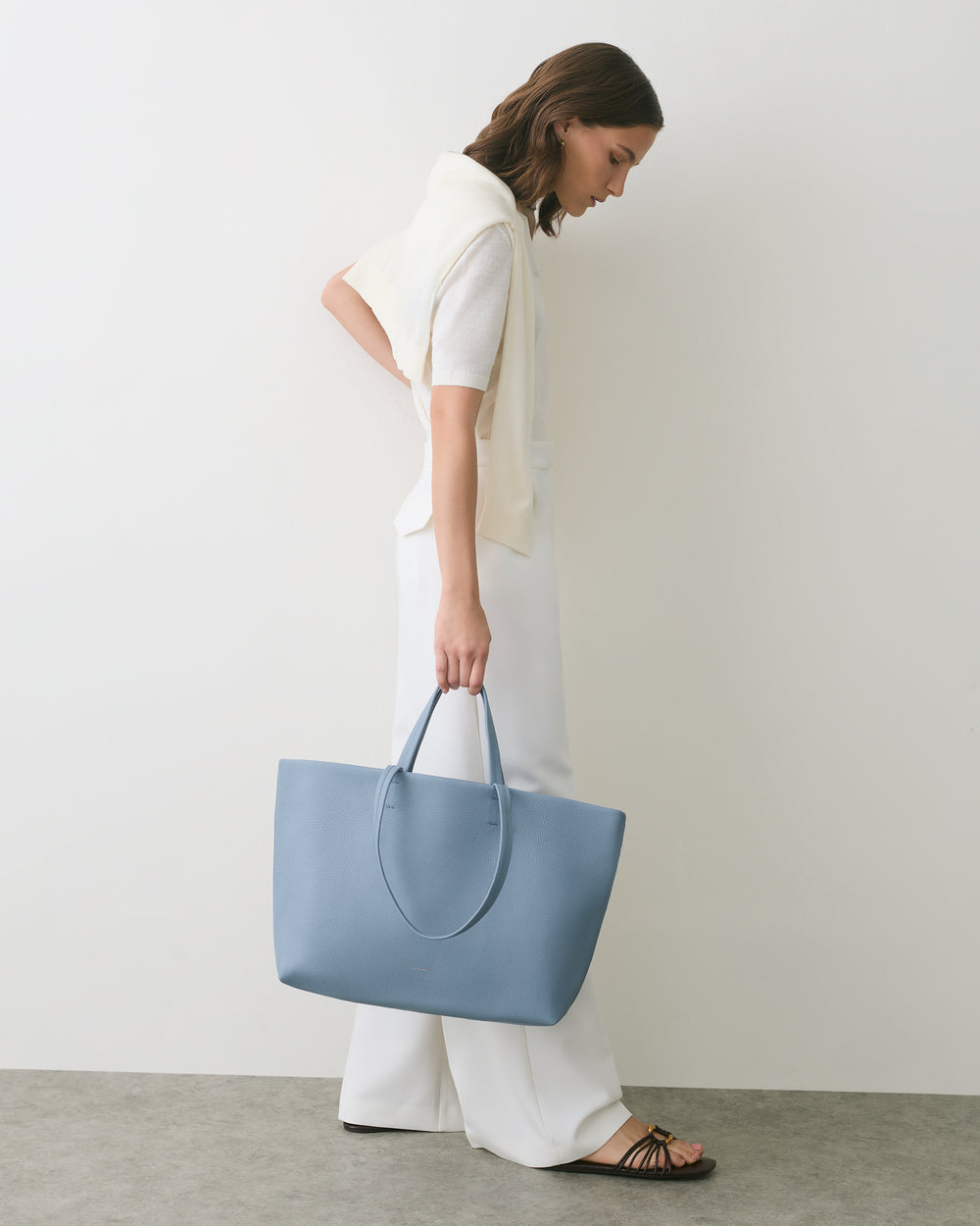 Person in profile holding a large tote bag, wearing casual clothing.