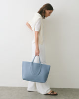 Person in profile holding a large tote bag, wearing casual clothing.