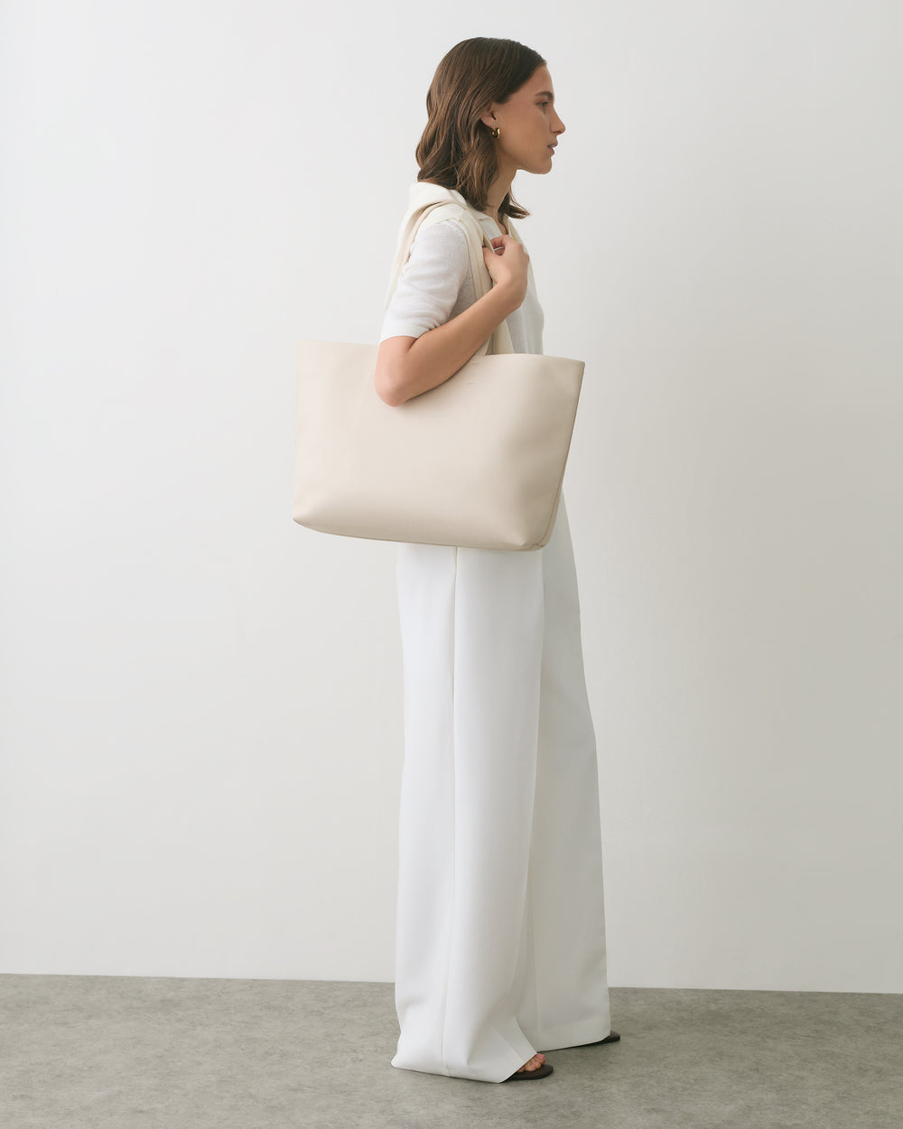 Person in white outfit carrying a large shoulder bag.