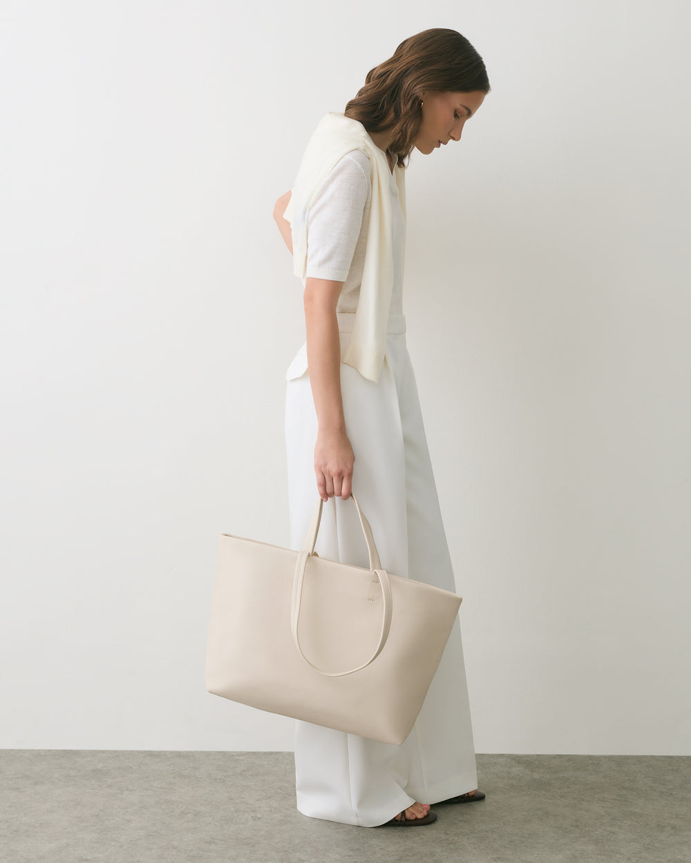 Person standing sideways holding a large tote bag