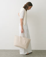 Person standing sideways holding a large tote bag