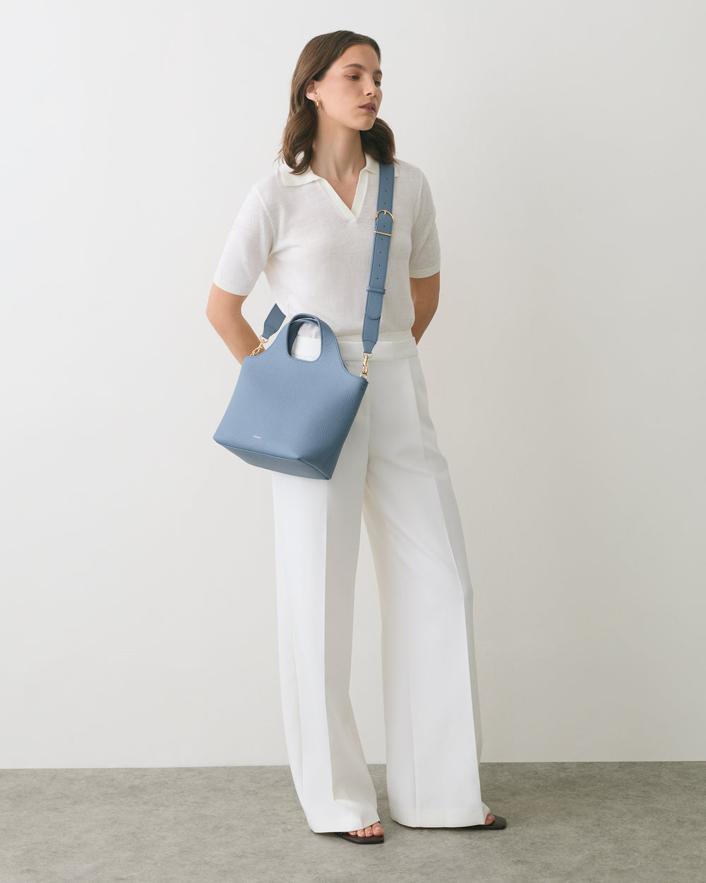 Person standing with a shoulder bag wearing pants and a short-sleeve top.