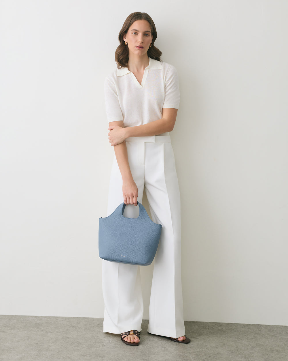 Person in white outfit holding a blue handbag.