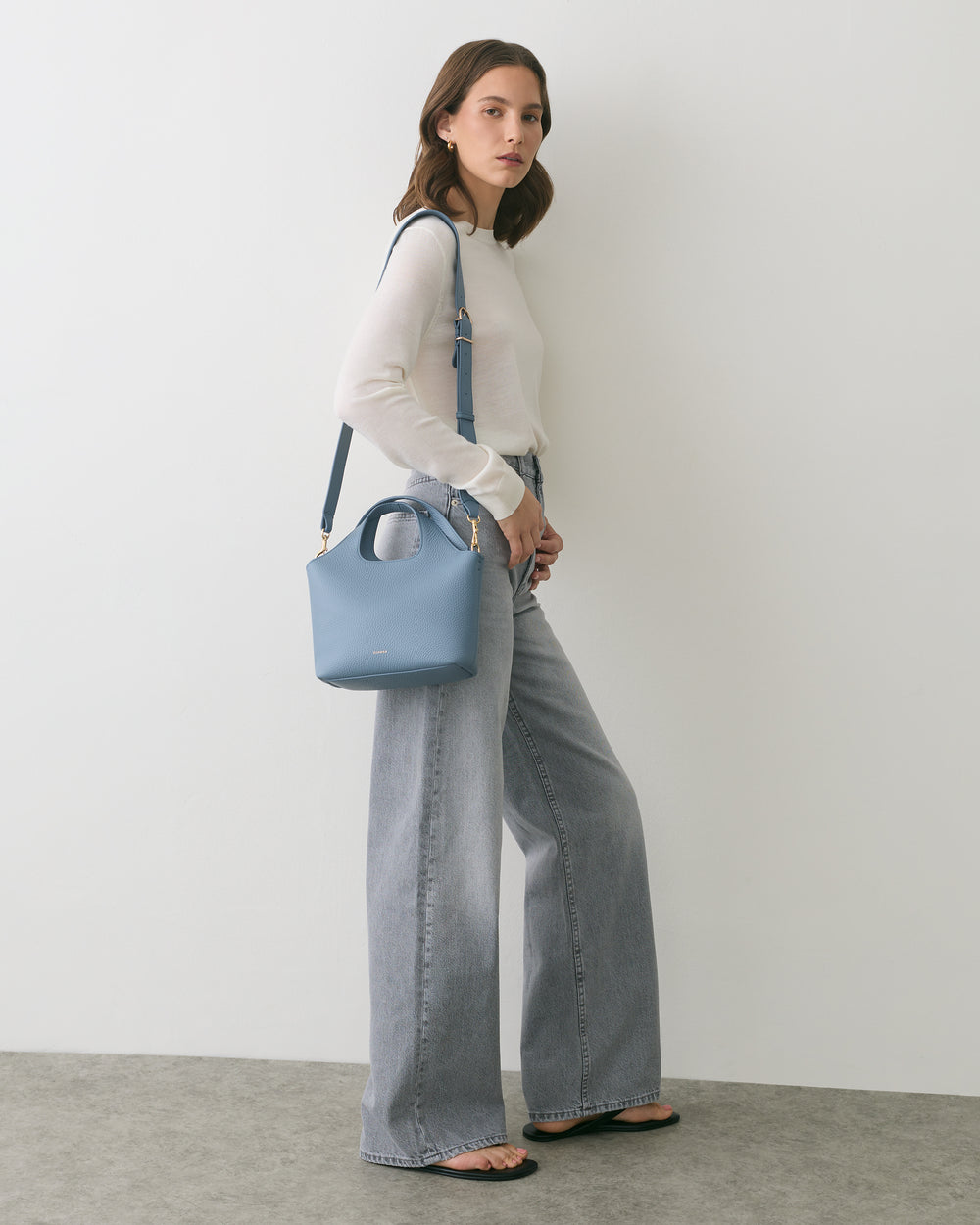 Person standing with a shoulder bag, wearing wide-leg pants and sandals.