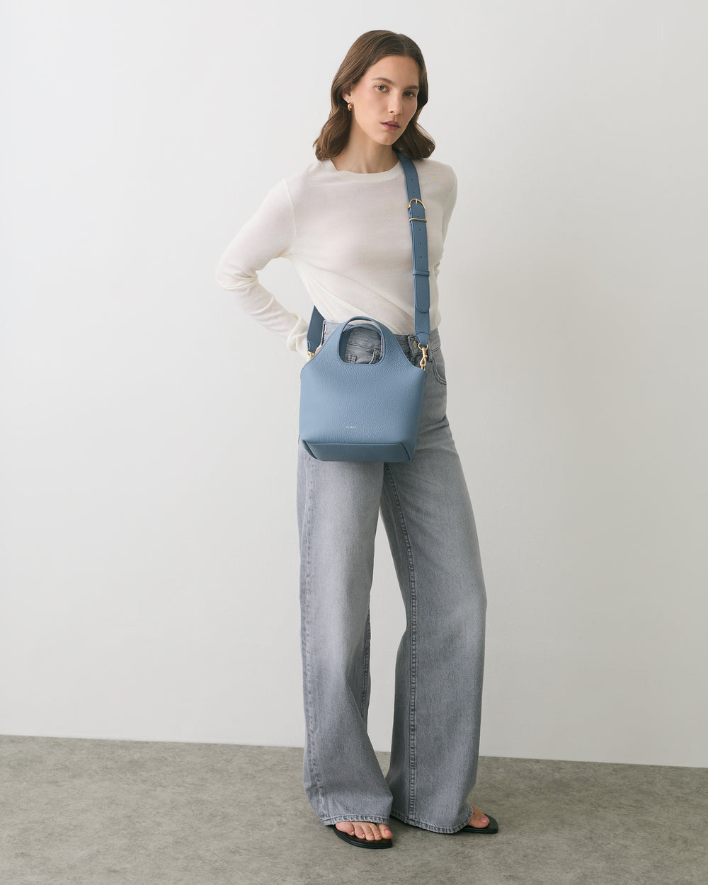 Person with shoulder bag wearing long-sleeve top and wide-leg jeans standing indoors.
