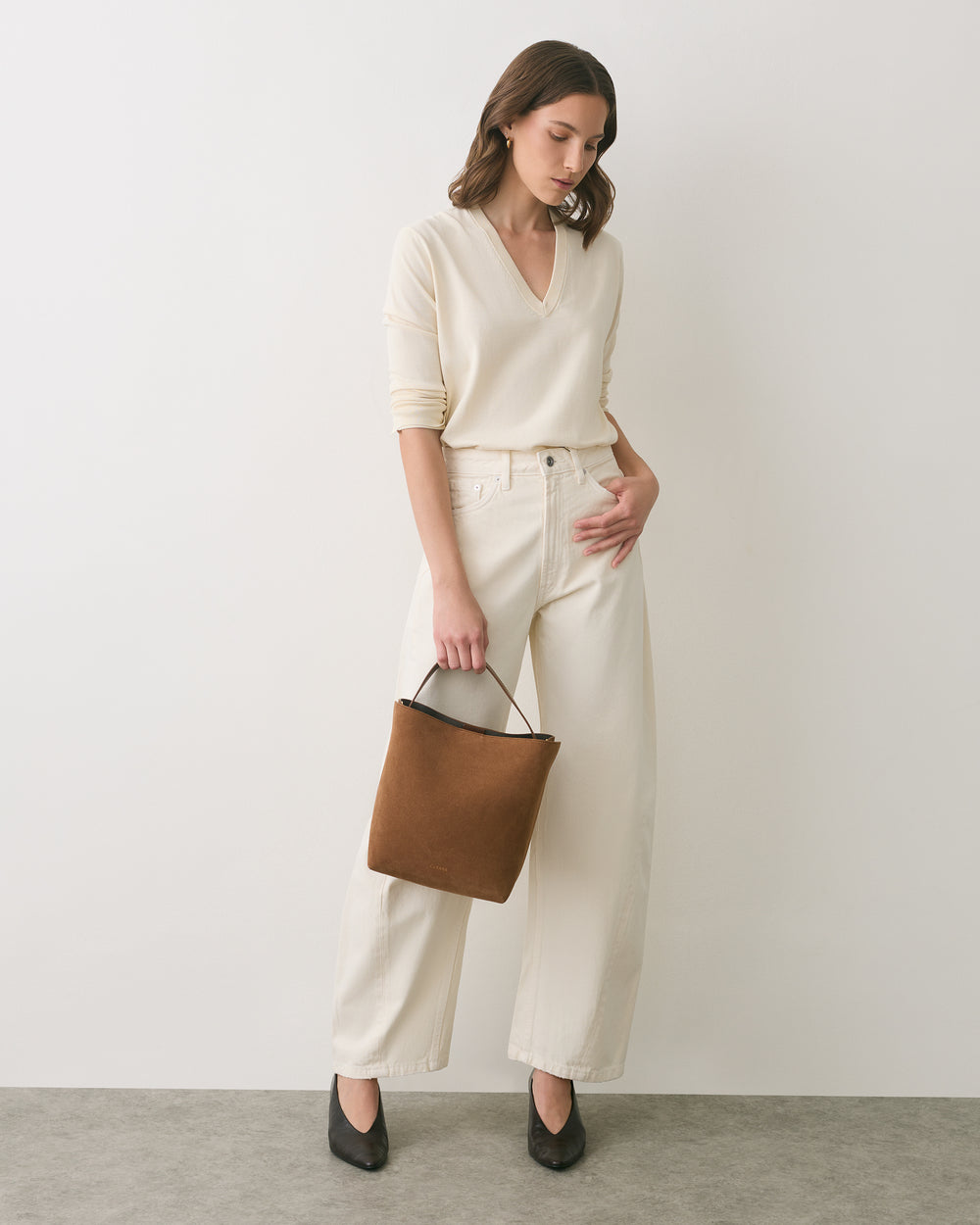 Person in a long-sleeve top and pants holding a square bag, standing against a plain background.