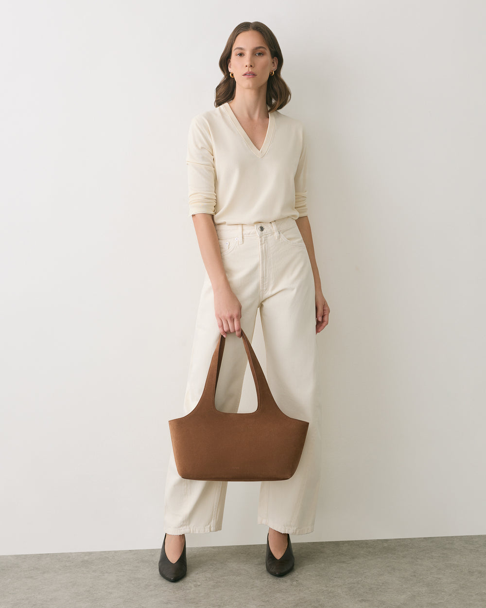 Person standing with a handbag, wearing a long-sleeve top and wide-leg pants.