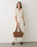 Person standing with a handbag, wearing a long-sleeve top and wide-leg pants.