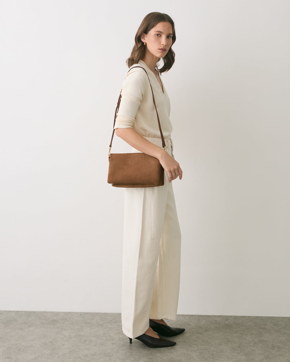Person standing with a shoulder bag wearing a sweater and trousers.