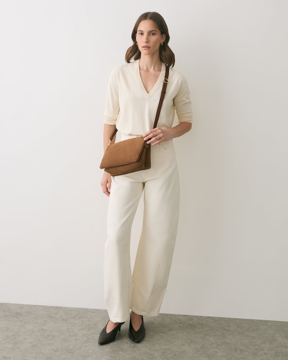 Person in matching outfit with shoulder bag standing indoors.
