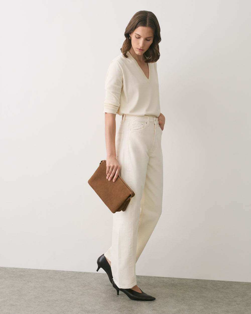 Person in top and jeans holding clutch, standing in heels looking down.