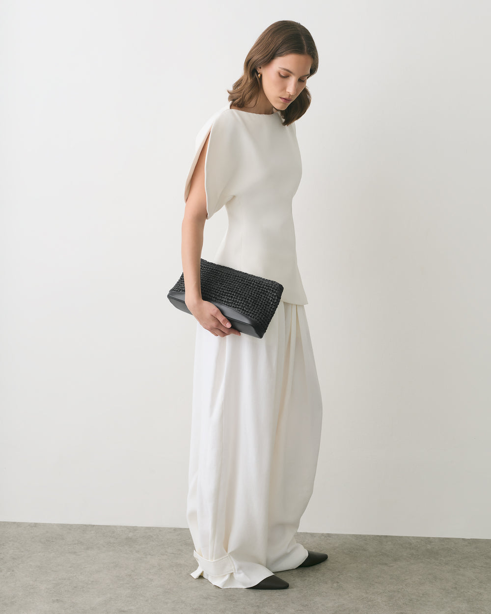 Person in a sleeveless top and wide pants holds a woven clutch