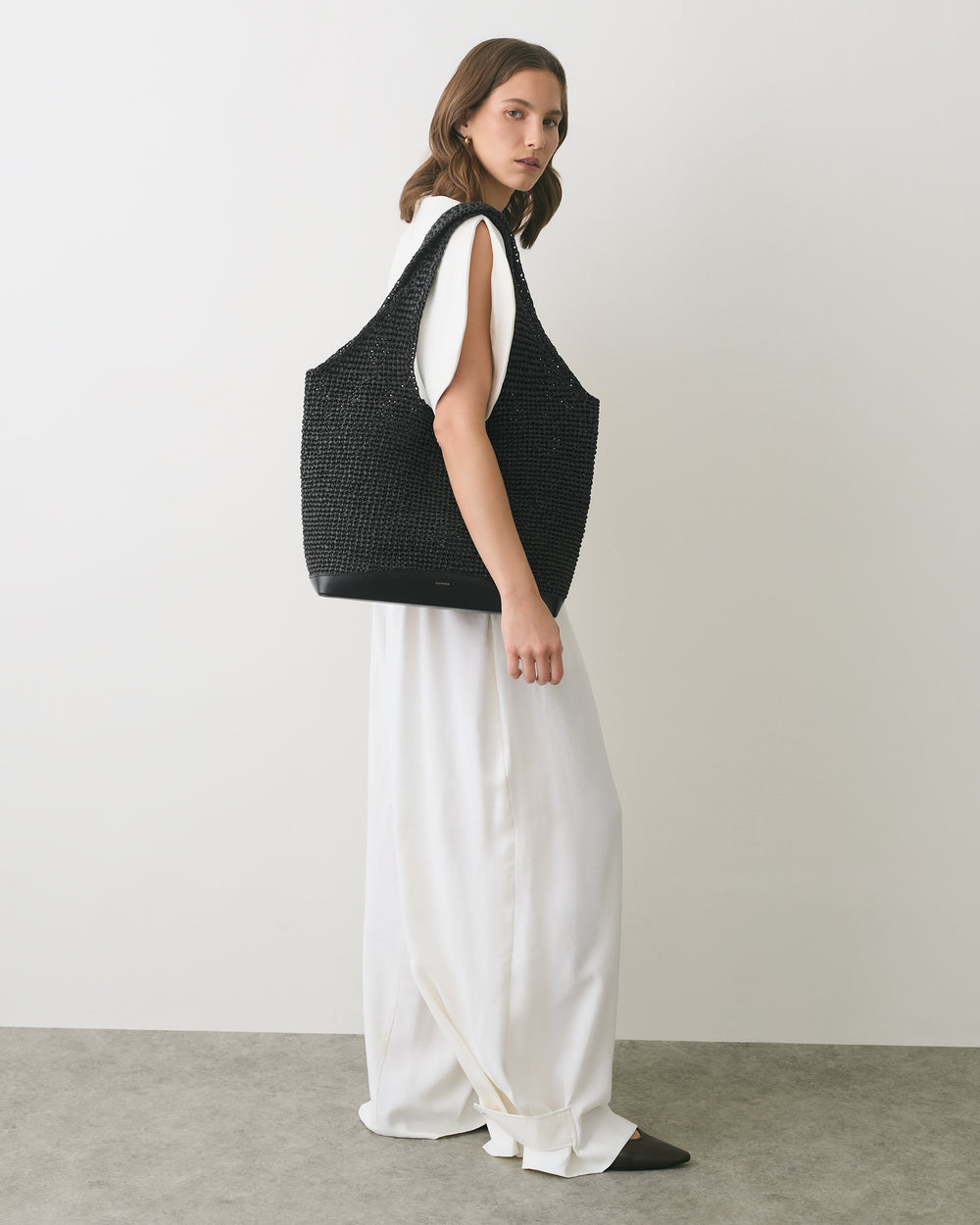 Person wearing white pants holding large woven tote bag