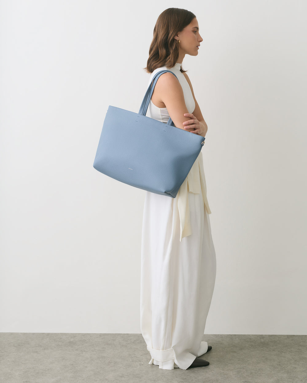 Person in a long dress holding a large tote bag on shoulder