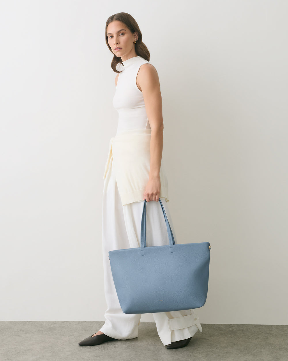 Person holding a large handbag, wearing a sleeveless top and wide-leg pants.