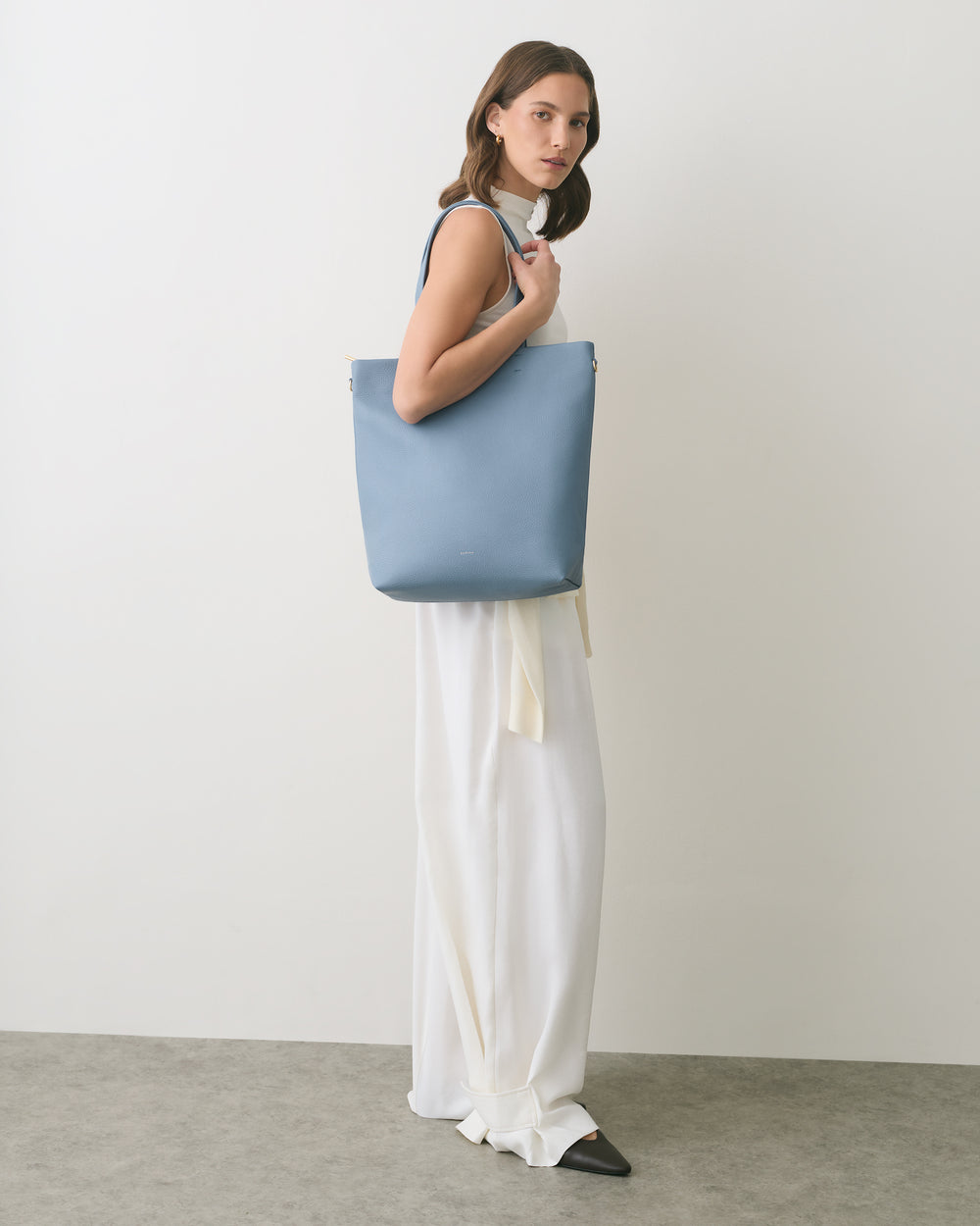 Person wearing a large bag over their shoulder, wearing a long dress.