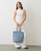 Person in sleeveless top holding a tote bag, wearing wide-leg pants.