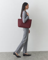 Person holding large tote bag, wearing sweater and jeans, standing sideways.