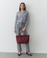 Person standing with a large tote bag, wearing a button-up shirt and jeans.