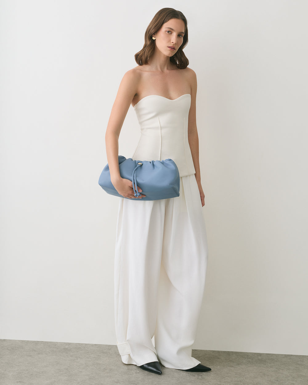 Person in strapless top and wide pants holding a handbag.