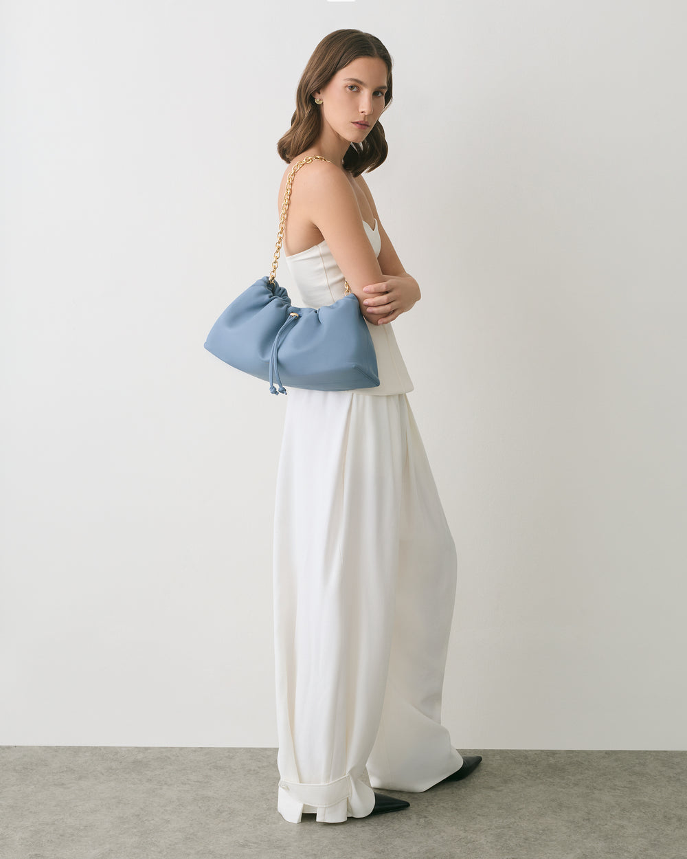 Woman in a long dress holding a chain strap clutch bag.