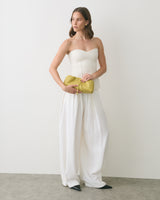 Person in strapless top and wide pants holds a bow-shaped clutch.
