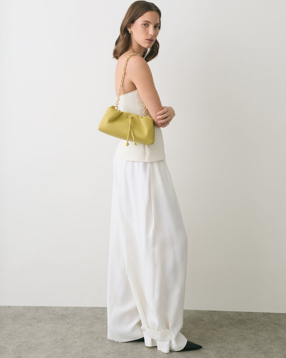 Woman in a white outfit holding a handbag with a chain strap.