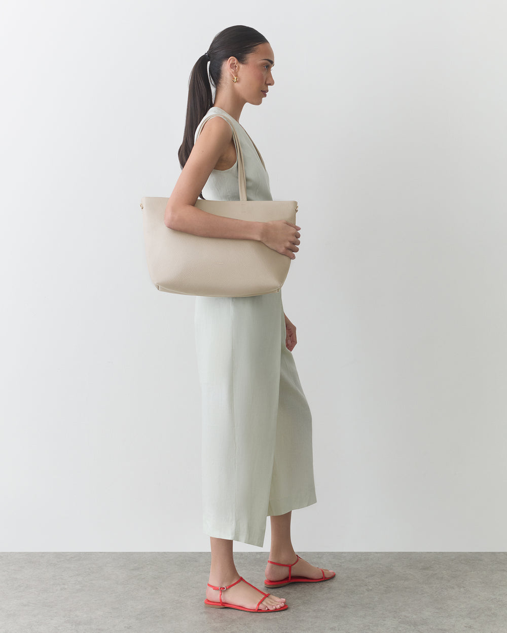 Person in a sleeveless jumpsuit holding a shoulder bag, wearing sandals.